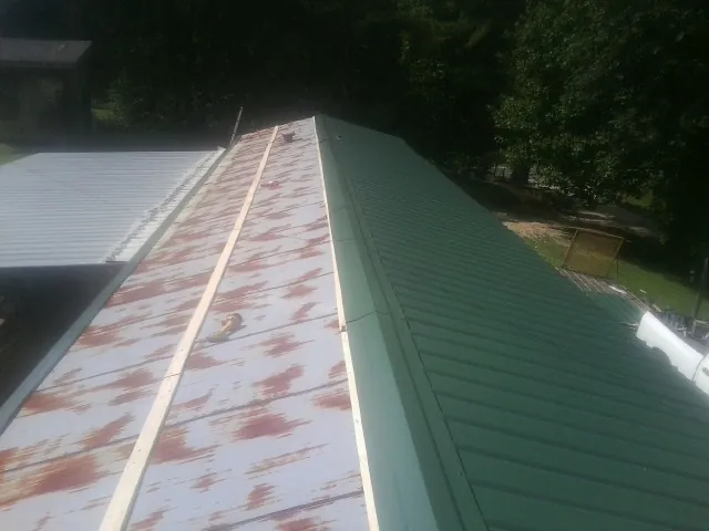 Old rusted panels beside newly installed green metal roofing — Wind Damage Roof Repair by Roofing Brothers in Walton